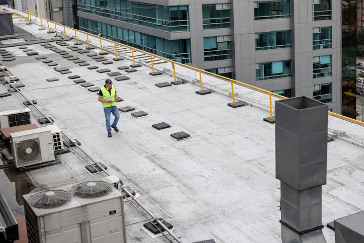 A person in a yellow safety vest inspecting a flat rooftop in Piperton, TN.
