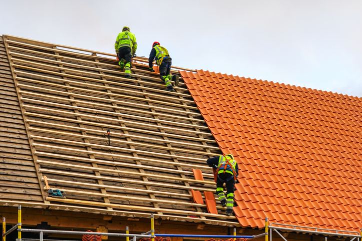 Three workers installing orange ceramic tiles on a steep roof in Senatobia, MS