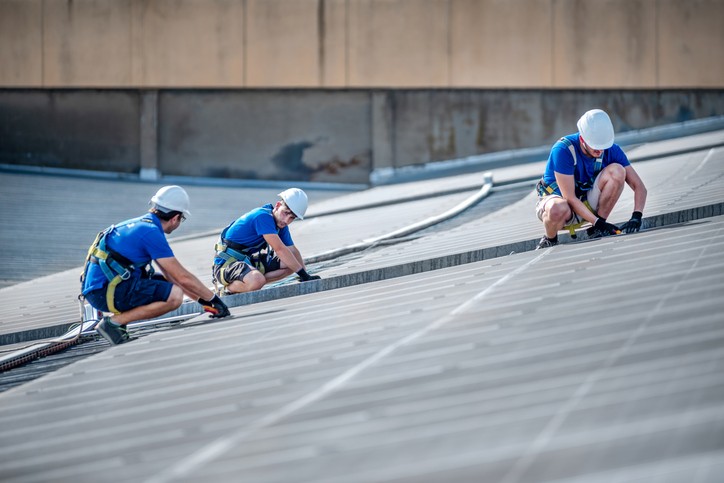 Three workers performing roof maintenance on a sloped industrial roof in Tunica, MS